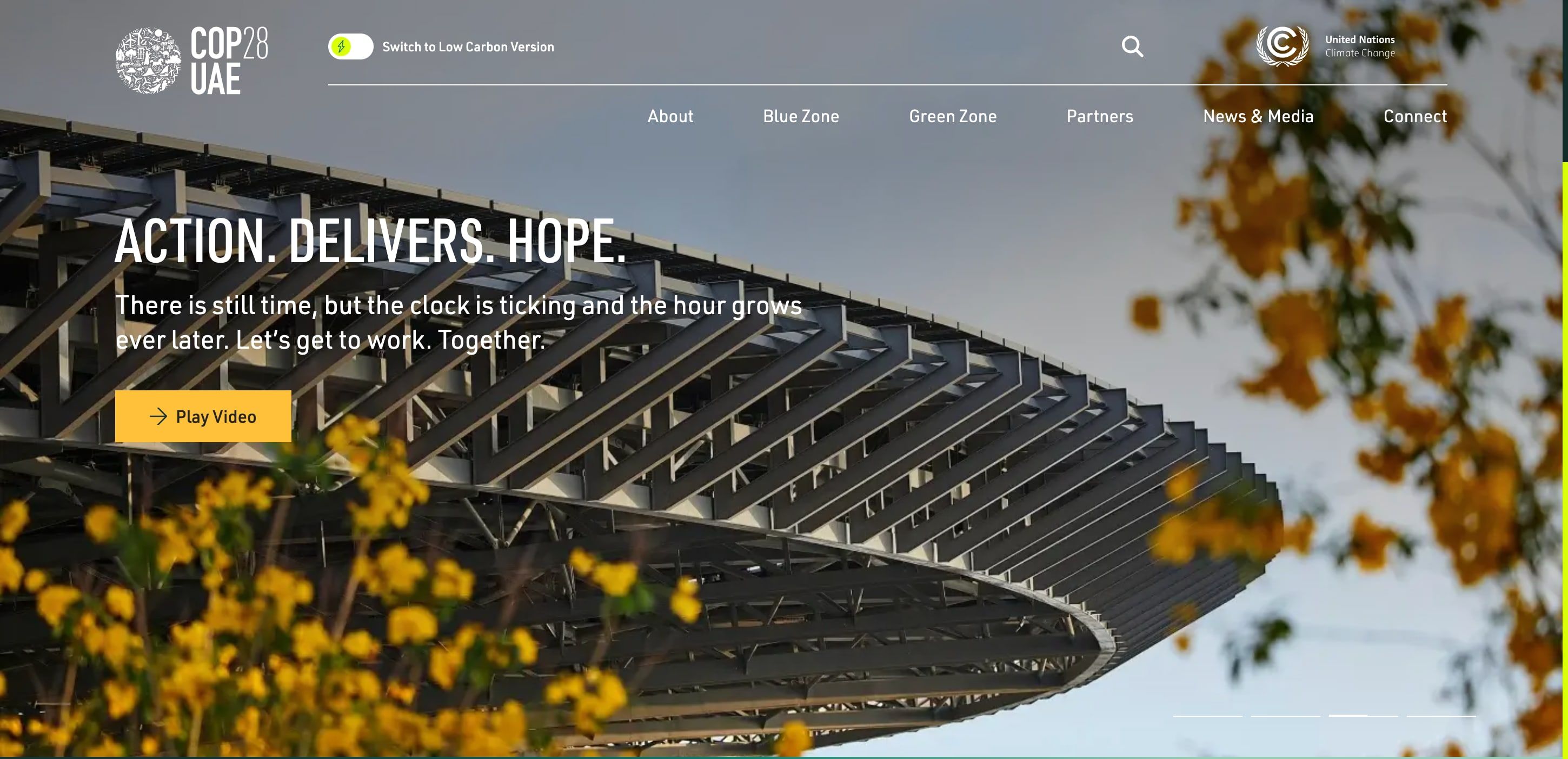 A screenshot of the COP28 homepage. It features a large background image of the edge of a rounded building. The overlaying heading text reads: Actions. Delivers. Hope. In the top left of the page is a toggle which says